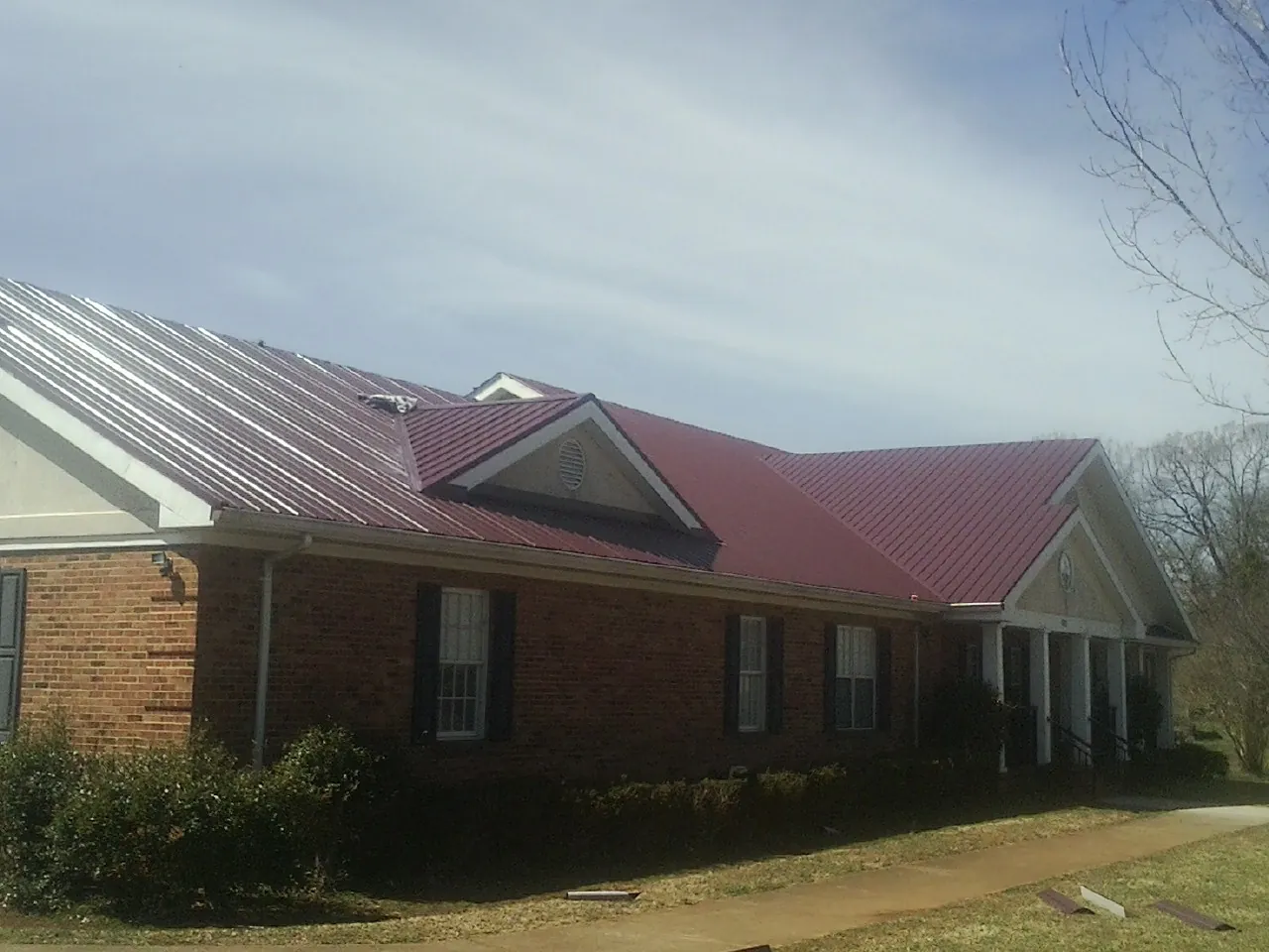 Red metal roof with gabled entries on a long brick building, from a Hail Damage Roof Repair job in Batavia