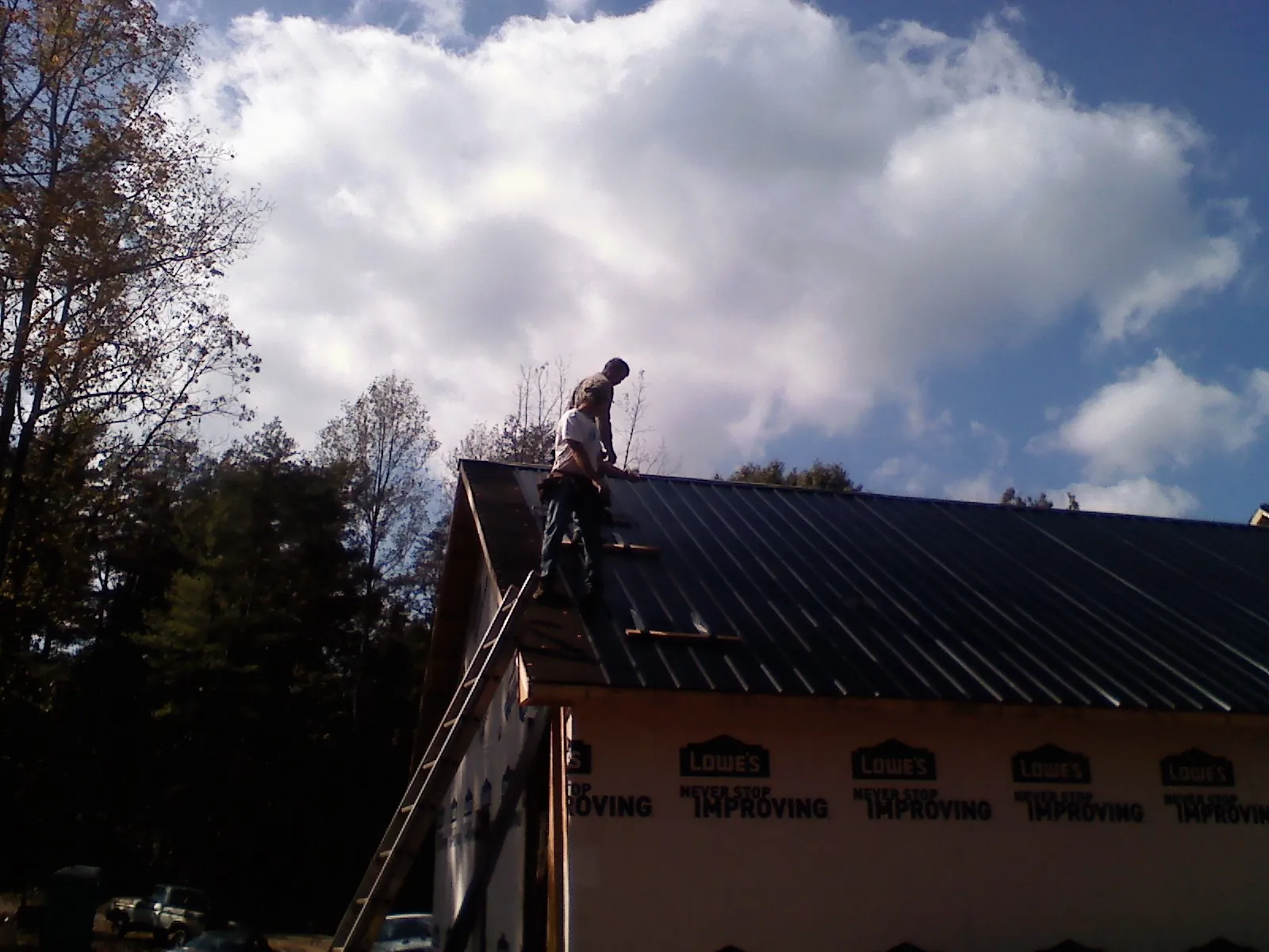 Roofer fastening dark metal panels high against a cloudy sky, from a Roof Inspection job in Batavia