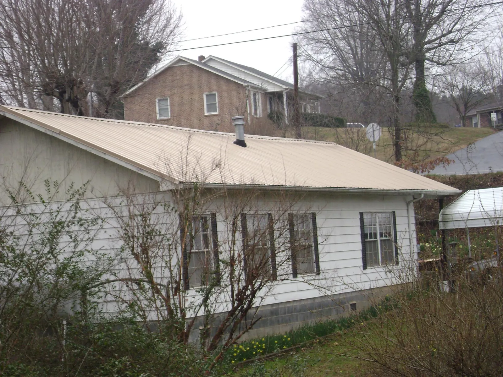 Tan metal roof on a white sided house set into a hillside — Commercial Roofing by Roofing Brothers in Batavia